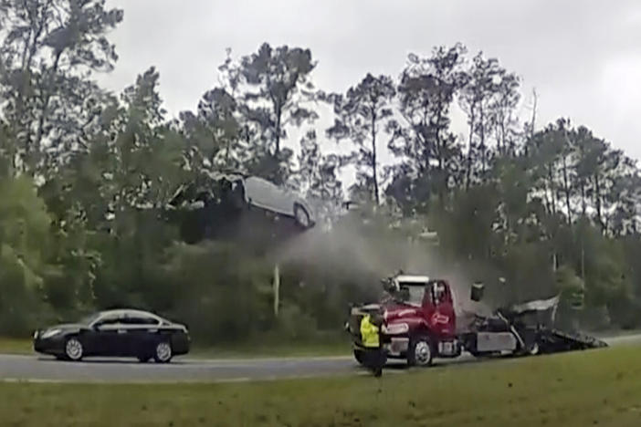 In this image taken from police body camera video provided by the Lowndes County, Ga., Sheriff's Office, a vehicle goes airborne after driving up the ramp of a flatbed tow truck on a Georgia highway, Wednesday, May 24, 2023, in Lowndes County, Ga. The Nissan Altima was launched 120 feet (37 meters) down the highway, according to a police report. The driver, a 21-year-old woman from Florida, was taken to South Georgia Medical Center with serious injuries. 
