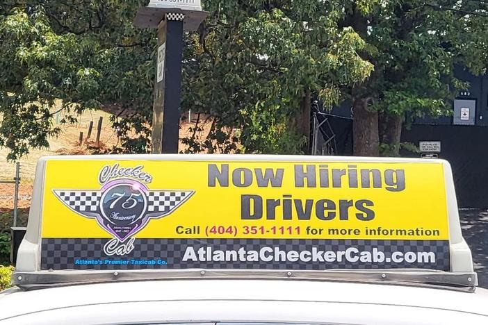 The sign on top of a yellow taxi cab is shown reading "Now Hiring Drivers."