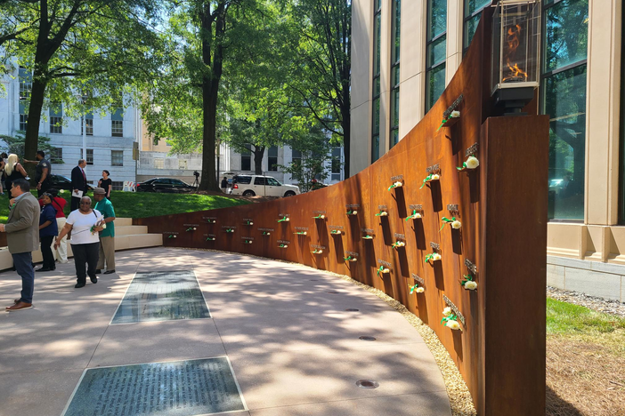 The memorial features a 55-foot steel wall with the names of the 30 victims in white with roses placed in front of them, mostly children, killed between 1979 and 1981 as well as a burning flame.