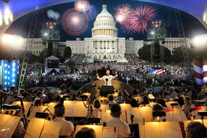 An orchestra playing with fireworks over the U.S. Capitol building.