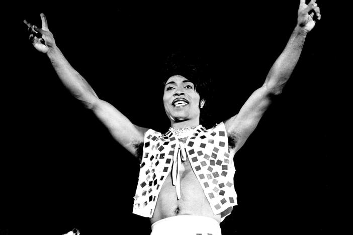 LITTLE RICHARD - US rock musician arms in air doing peace sign in glitter vest.