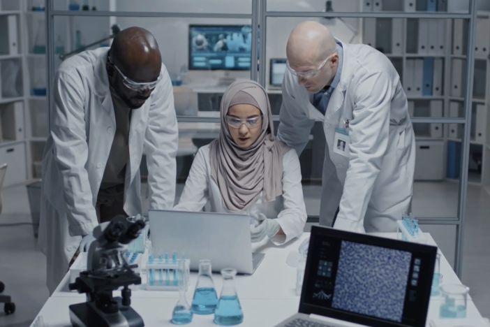 A diverse group of scientists discuss over a laptop and microscope.