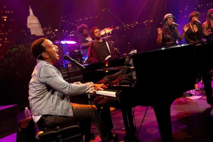 John Legend on stage singing and playing piano.