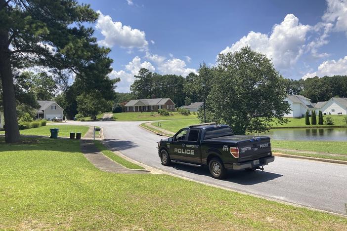 A police vehicle stands guard in the Dogwood Lakes neighborhood in Hampton, Ga., on Sunday, July 16, 2023. Police say a man who lived in the brick house in the background shot and killed four people in the neighborhood on Saturday, July 15.