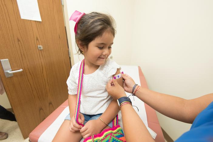 A young girl has a bandage placed on her arm after receiving an immunization.