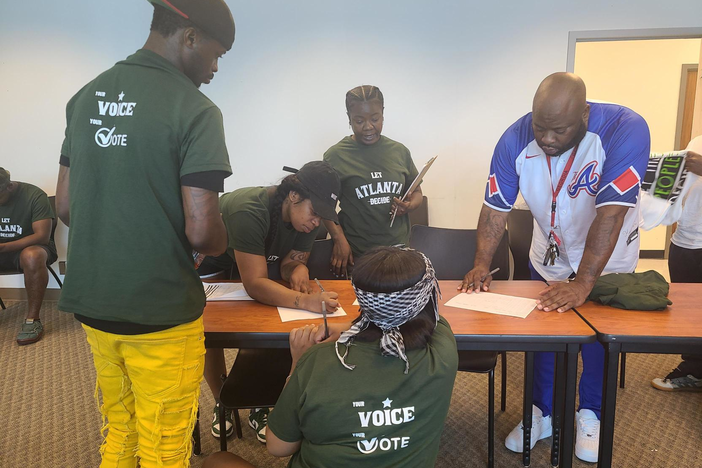 Four volunteers in green shirts, and one in a blue baseball jersey, with the Black Male Initiative sign up for different locations to canvas on July 27, 2023. 