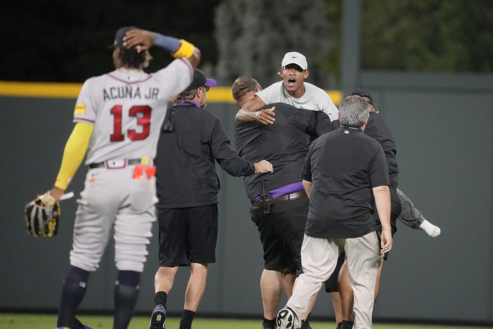 Field guards haul away one of two fans who approached Atlanta Braves right fielder Ronald Acuna Jr. (13) before the bottom of the seventh inning of a baseball game against the Colorado Rockies, Monday, Aug. 28, 2023, in Denver. 