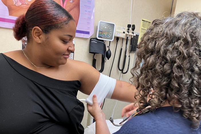 A woman has her arm bandaged by a nurse.