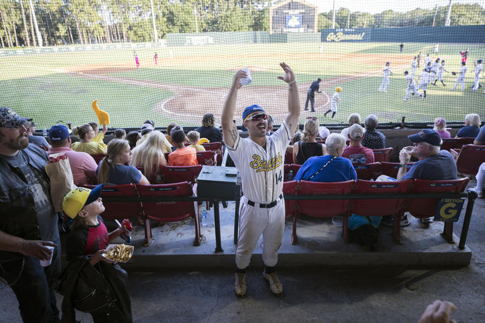 Savannah Bananas catcher Vinny Rauso, center, tries to get fans to cheer before throwing a free T-shirt to the loudest section, during the team's baseball game against the Florence Flamingos, June 7, 2022, in Savannah, Ga. A new exhibit dedicated to the sport's wackiest team, the Bananas, will open Friday at the Baseball Hall of Fame in Cooperstown, N.Y. 