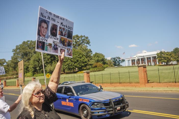 Carrie Proffitt protests Tuesday across from the Georgia Governor's Mansion with photos of her son who took his own life in a Georgia Department of Corrections prison this year.