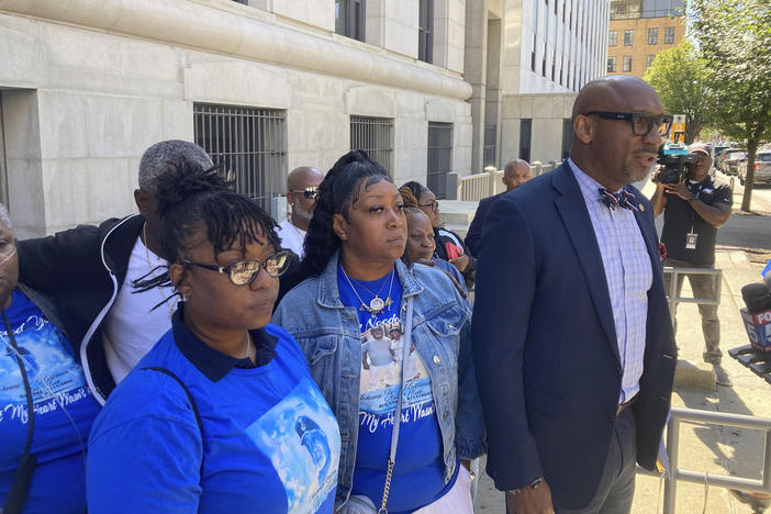 Attorney Mawuli Davis, right, speaks to reporters, Monday, Oct. 9, 2023, outside the Fulton County courthouse in Atlanta, while flanked by relatives of Johnny Hollman Sr.