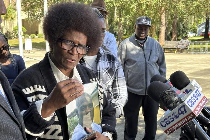 Mary Cure is shown holding a picture of her son Leonard Cure as she speaks in front of microphones,