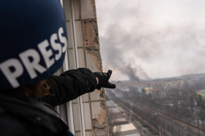 A reporter pointing out a window towards an explosion.