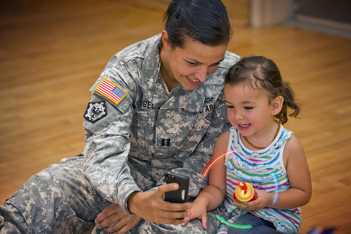 A military servicemember holds a cellphone up for a child