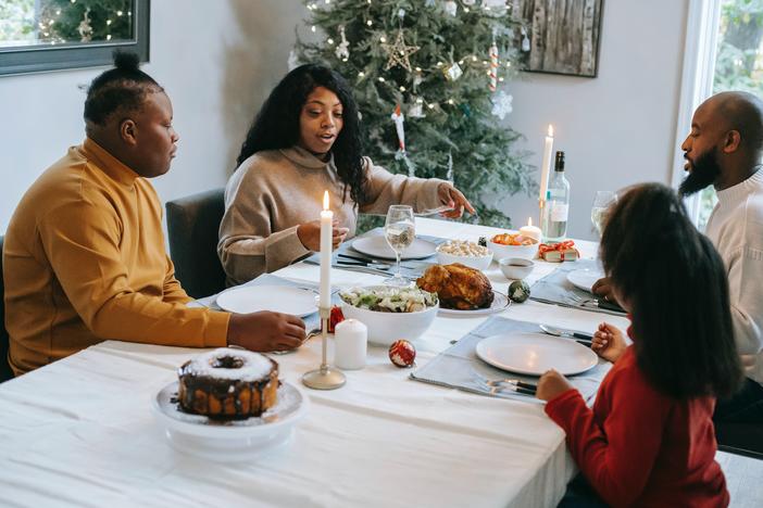 A Black family seated around a table with a Christmas tree in the background