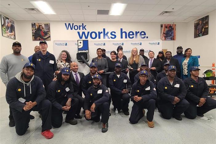 Students of the first Clean Tech Infrastructure Academy cohort gather at the Goodwill to celebrate completing the program January 23, 2024. They each have on blue work jumpsuits and blue hats.