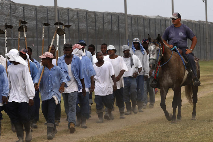 In this Aug. 18, 2011 photo, a prison guard rides a horse alongside prisoners as they return from farm work detail at the Louisiana State Penitentiary in Angola, La. After the Civil War, the 13th Amendment's exception clause, that allows for prison labor, provided legal cover to round up thousands of mostly young Black men. They then were leased out by states to plantations like Angola and some of the country's biggest privately owned companies, including coal mines and railroads. 