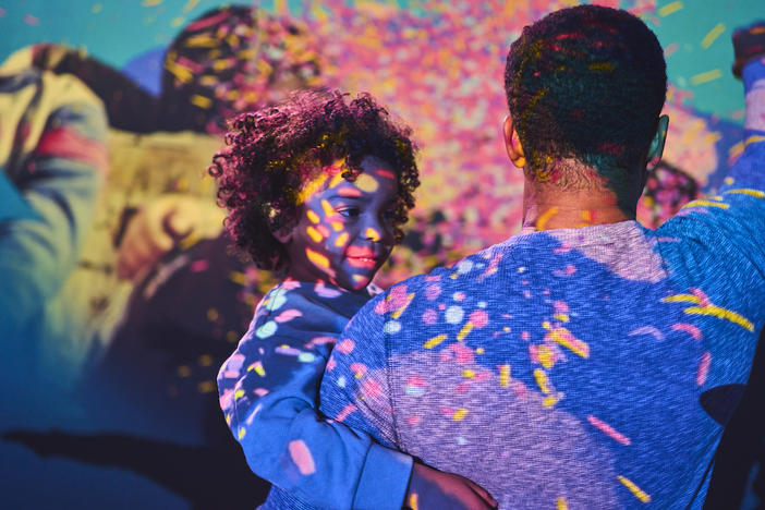 A child and adult dance together in the immersive light experience in the "Our Song" station of UNICEF's Heartstrings exhibition. 