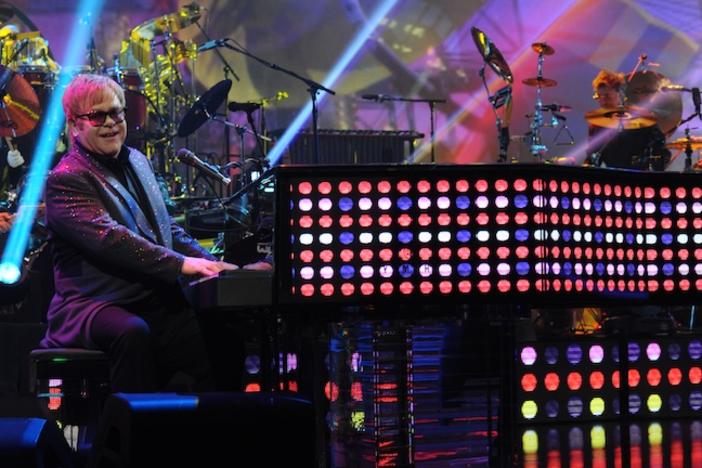 Elton John playing a piano wrapped in LED