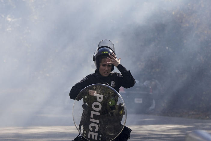 A police officer runs out of a cloud of gas during a demonstration in opposition to a new police training center, Monday, Nov. 13, 2023, in Atlanta. 