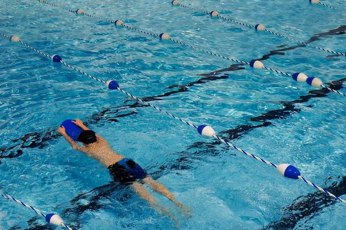 A boy holding a kickboard swims in a swimming pool lane