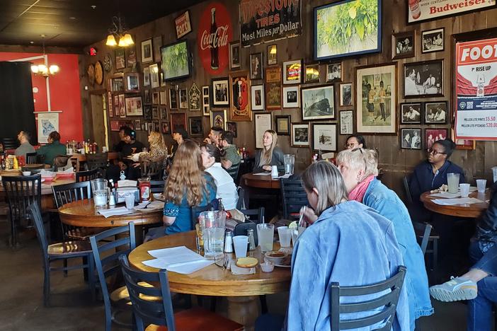People sitting in chairs with a wall of photos and art in the background