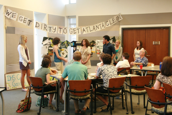 people sitting and standing around a table with a banner in the background that says, "we get dirty to get Atlanta clean."