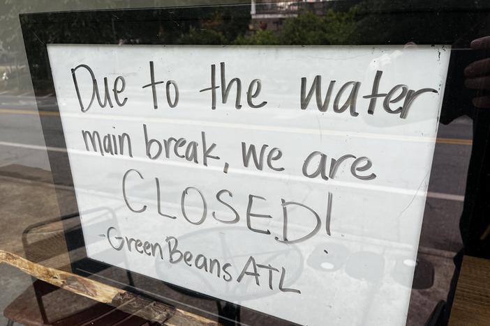 A sign, seen through a window, says "Due to the water main break, we are CLOSED! Green Beans ATL."