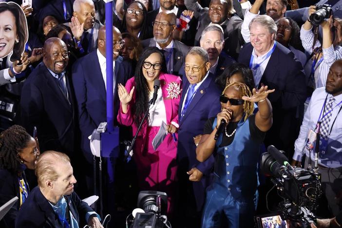 A group of people, including Atlanta Congresswoman Nikema Williams and rapper Lil Jon, are show on the floor of a convention hall.