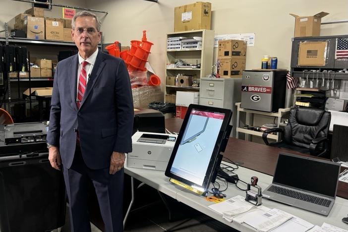 Secretary of State Brad Raffensperger stands with a voting machine