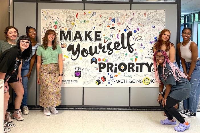A group of students at Kennesaw State University stand with a sign that says "make yourself a priority"