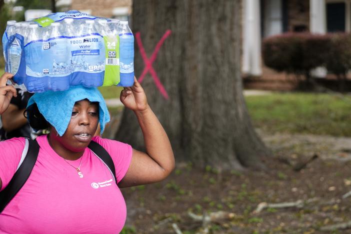 Shaday Collins balances bottled water on her head for a miles long walk back home from one of the Augusta distribution sites.