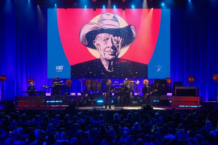 A performer on stage in front of an image of President Jimmy Carter.
