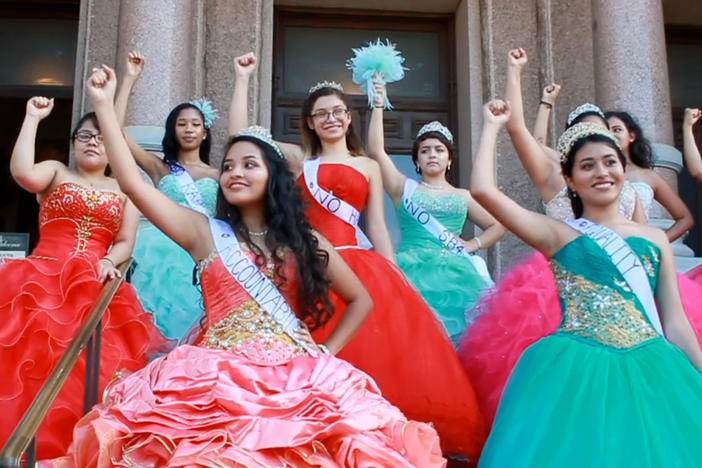 A group of teenage girls in dresses raising their fists.