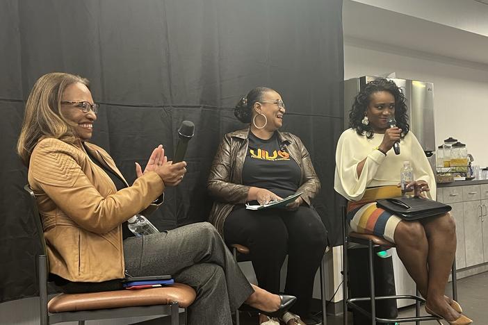 Acting Secretary Todman sits on a chair against a black background with two other black women of Caribbean descent in Norcross.