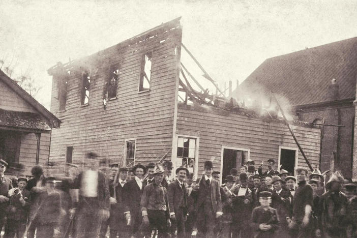 A mob standing in front of a burning building in a sepia photo.