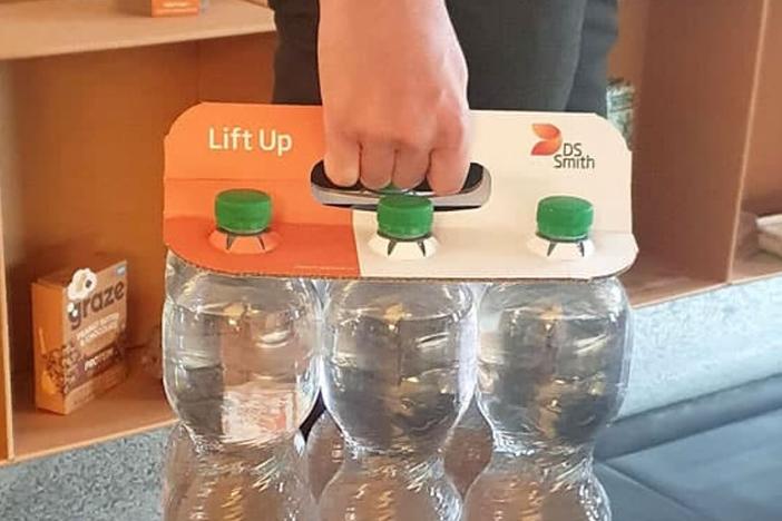 A six-pack of plastic water bottles is shown being held together by a paper-based holder.