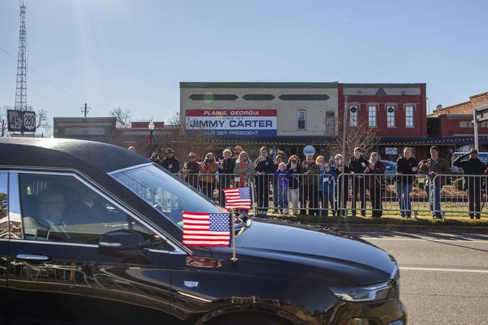 The hearse carrying the body of former president Jimmy Carter passes people who gathered to pay respects in Plains, Ga. Saturday. (Grant Blankenship/GPB News)