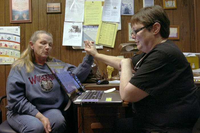 Two women sit holding hands with a laptop between them