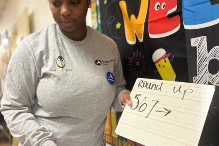 A young woman is shown in a classroom holding a sign that says "Round up 567."