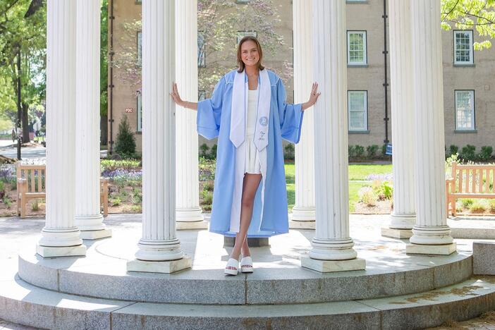 Ruth McCrady stands outside in a blue graduation robe