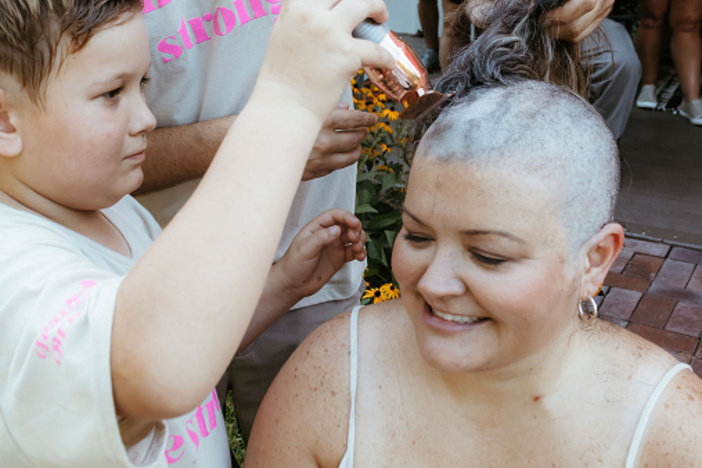 A man and a boy shave a woman's head