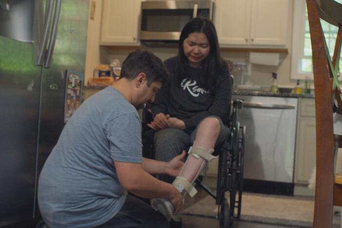man kneeling by woman in a wheelchair, helping her with a brace on her leg