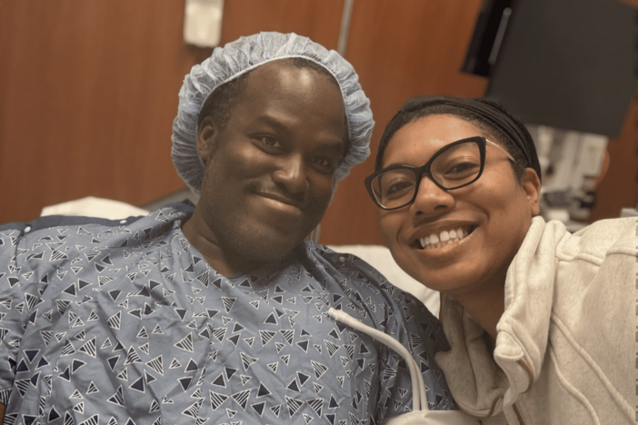 A man sits in a hospital bed with his wife by his side. 