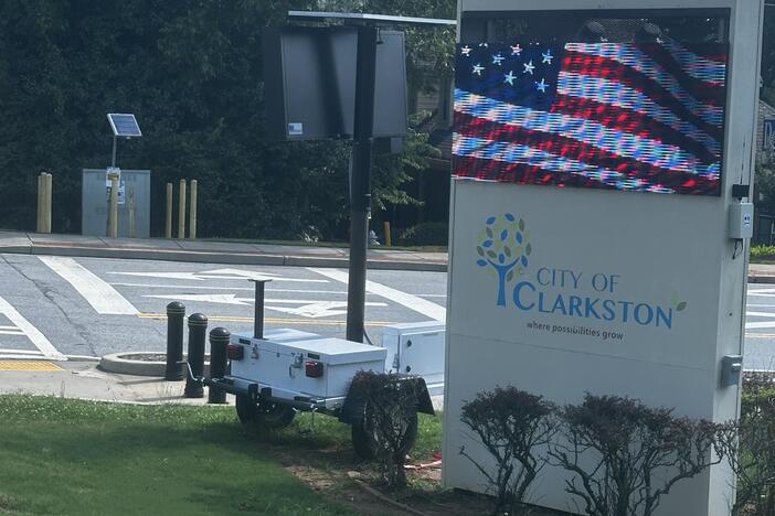 An LED screen shows a waving American flag on a welcome sign for the City of Clarkston. The text beneath reads "Where possibilities grow"