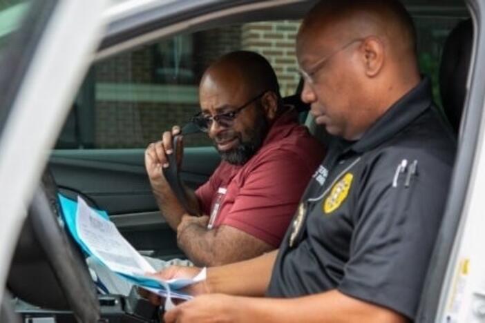 A law officer and another person sit in a car looking at papers