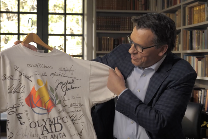 A former athlete holding up a shirt from the 1996 Atlanta Olympics.