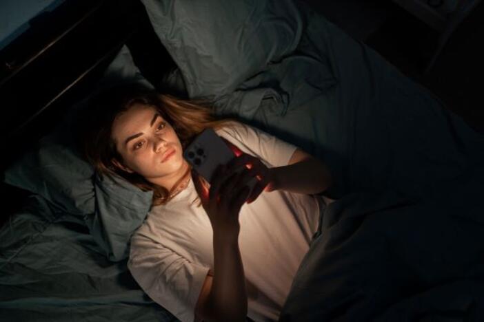 Sad girl bored in bed with mobile phone late at night in dark