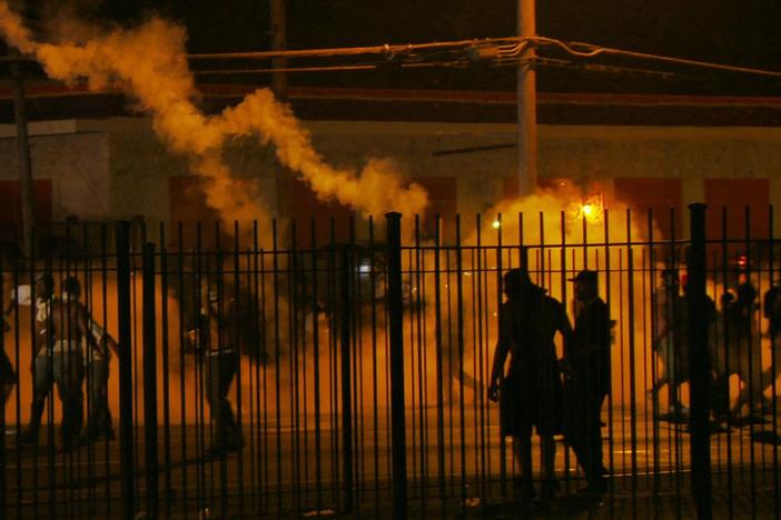 Clip shows police using military tactics to disperse a crowd of non-violent protestors.