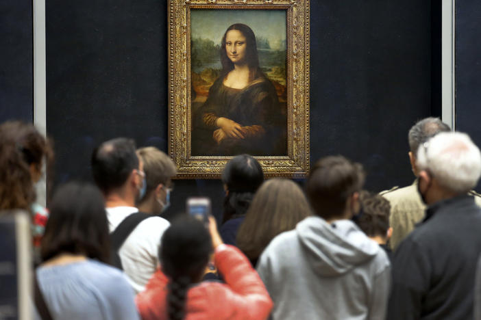 Visitors wearing face masks wait to see the <em>Mona Lisa</em> at the Louvre Museum on Monday. The most visited museum in the world reopened to the public after closing in March.